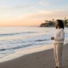 A person stands calmly on a quiet beach at golden hour watching gentle Pacific waves roll in, looking settled and at ease