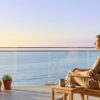 A person sits quietly on a light-filled balcony overlooking a calm Southern California view, taking a reflective pause