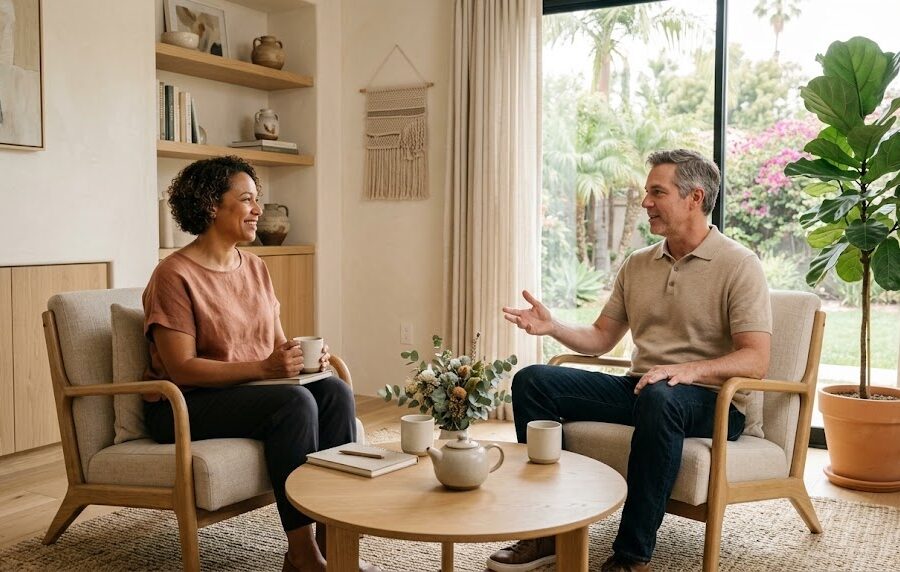 Two people talk across a low table in a sunlit, softly furnished consultation room with a calm California feel