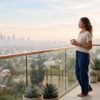 A person stands quietly on a balcony above a soft California cityscape in early morning light